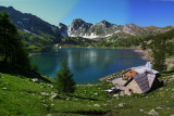 Wide view of Lake Allos and its mountains in the background, as well as the refuge on the right with its terrace, tables and chairs