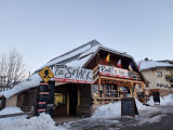 Vue d'ensemble du restaurant, bâtiment en bois sur deux étages avec deux entrées, terrasse extérieure. Panneaux 