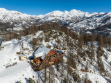 Vue du restaurant d'altitude en drone, chalet en bois et pierre au milieu des montagnes enneigées, terrasse en bois