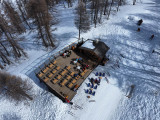 Drone view of the restaurant, chalet and wooden terrace in the middle of the slopes and forest, tables and chairs, deck chairs