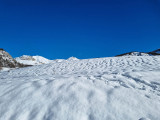 A vast, rolling, snow-covered landscape, snow-capped mountains in the background, a vast blue sky
