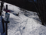 The snowshoe trail starts at the Valdemars Forest House, marked by a purple trail sign and an altitude marker. The trail winds through a forest in winter, covered in snow.