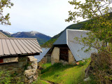 Hameau de Chaumie, sentier de terre et d'herbes sinuant entre les petites maisons anciennes en pierre aux portes larges et toits en tôle. Montagnes en arrière-plan