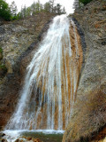 Cascade de Chaumie, cascade rocheuse se déversant depuis une forêt de conifères dans un petit bassin naturel creusé dans la roche