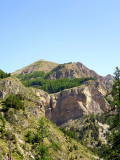 A distant view of the Pich waterfall, cascading down a rocky crevice, surrounded by forests both above and below