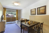 Bright apartment living room with sofa, TV unit, TV, dining table, French doors opening onto a balcony, view of the resort