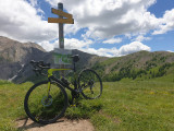 Mountain bike leaning against a hiking sign located at the Col d'Allos, the summit of the mountains visible all around