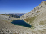 Lac de la Cayolle, grande étendue d'eau au milieu d'un promontoire rocheux à la végétation rare. Montagnes en arrière-plan