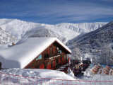 View from the restaurant, a wooden chalet with a terrace, tables and chairs, and long chairs. Snow-capped mountains all around and in the background.