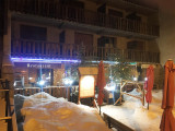 Night view of the crêperie's facade, located on the ground floor, with fir trees decorating the terrace, snow