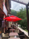 The restaurant's outdoor terrace, in a paved courtyard, with tables and chairs under red parasols.