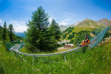 Luge sur rail Verdon Express, nacelle deux places, série de virages en épingle dans un cadre de végétation, vue dégagée sur les montagnes environnantes