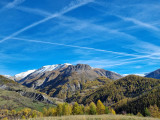 An unobstructed view of a colorful, wooded mountain valley. The mountain peaks in the background are snow-capped.