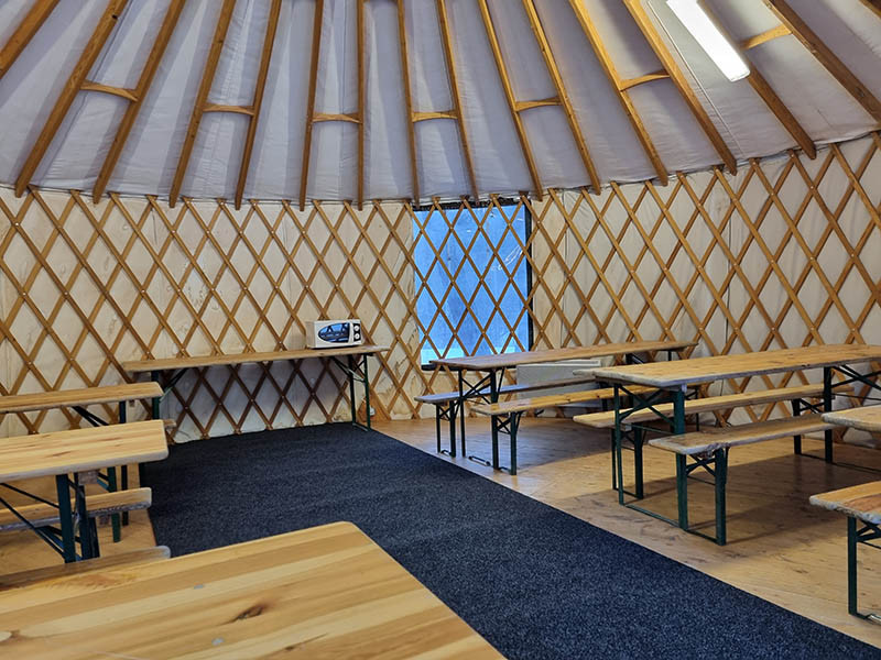Salle hors-sac de Val d'Allos - le Village, salle couverte en forme de yourte avec tables et chaises, micro-ondes - © B Courbon Salle hors-sac de Val d'Allos - le Village, salle couverte en forme de yourte avec tables et chaises, micro-ondes