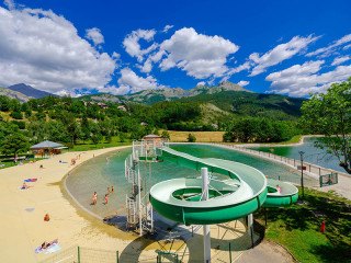 Bassin de baignade du parc de loisirs d'Allos, comportant un toboggan. En arrière-plan, montagnes boisées