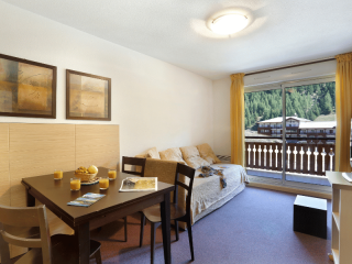 Bright apartment living room with sofa, TV unit, TV, dining table, French doors opening onto a balcony, view of the resort