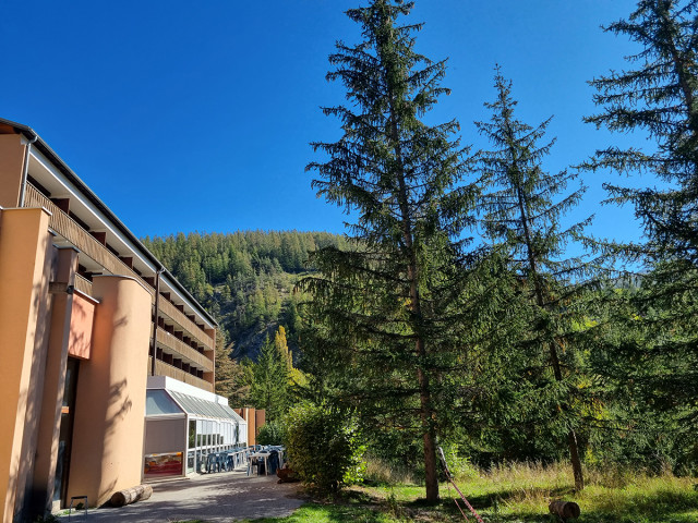 Vue de côté du centre de vacances sur plusieurs étages, avec terrasse proche d'une véranda, au milieu de la forêt