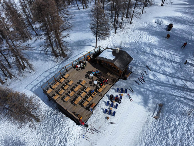 Drone view of the restaurant, chalet and wooden terrace in the middle of the slopes and forest, tables and chairs, deck chairs