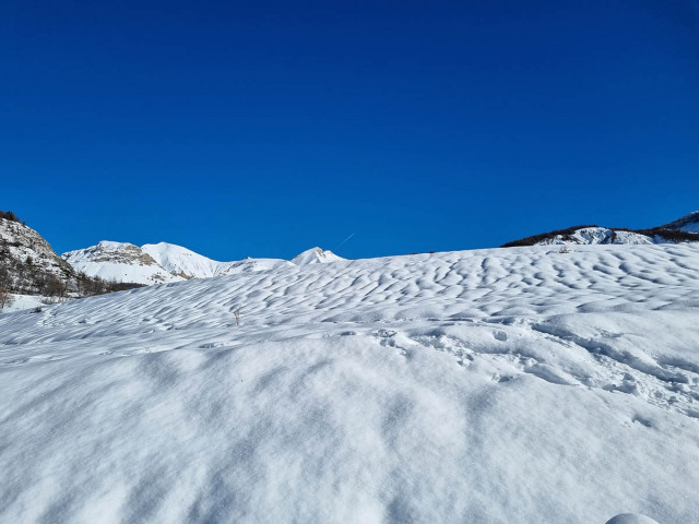 A vast, rolling, snow-covered landscape, snow-capped mountains in the background, a vast blue sky
