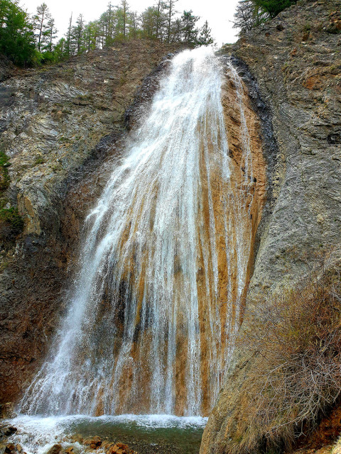 Cascade de Chaumie, cascade rocheuse se déversant depuis une forêt de conifères dans un petit bassin naturel creusé dans la roche