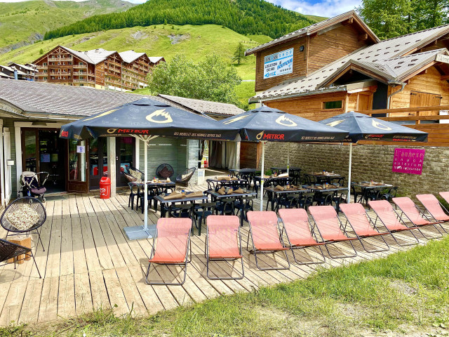 The establishment's terrace in summer featuring tables, chairs, parasols, and sun loungers, all situated amidst the resort and greenery.