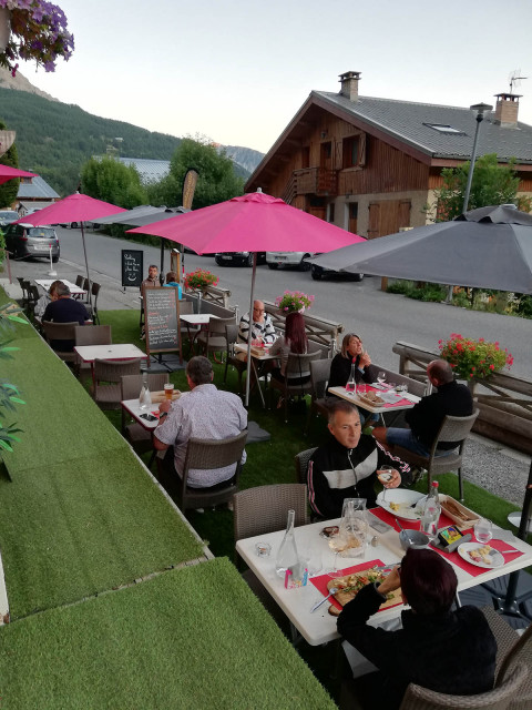 Terrasse extérieure avec sol en faux gazon, tables et chaises, parasols, grand-rue du village