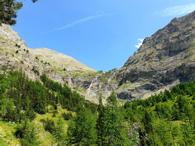 Front view of the Cimet Waterfall, a large cascade over a rocky outcrop facing a coniferous forest