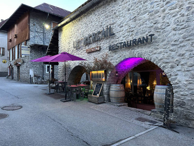 Restaurant located in a stone building with an entrance through a semicircular archway. Outdoor terrace, barrels used as decoration. Sign: 