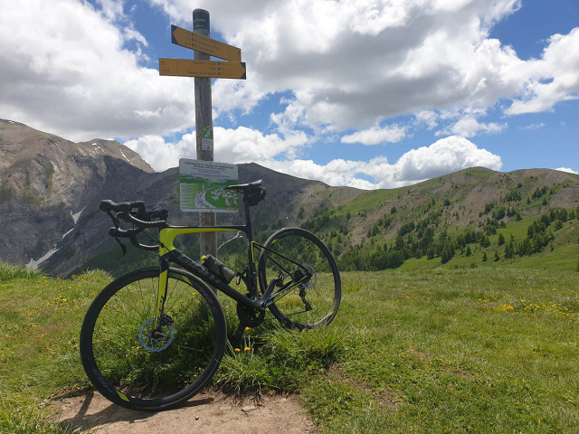 Mountain bike leaning against a hiking sign located at the Col d'Allos, the summit of the mountains visible all around - © B Courbon Mountain bike leaning against a hiking sign located at the Col d'Allos, the summit of the mountains visible all around