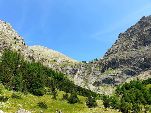 Front view of the Cimet Waterfall, a large cascade over a rocky outcrop facing a coniferous forest