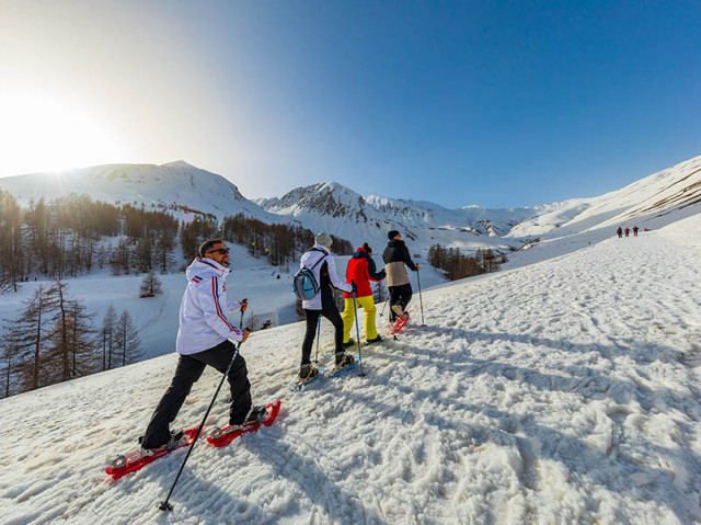 Randonneurs en raquettes montant le long du sentier de la cabane de Sestrière, cirque dégagé ensoleillé avec montagnes enneigées