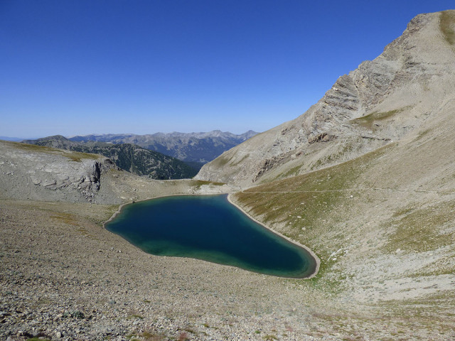 Lac de la Cayolle, grande étendue d'eau au milieu d'un promontoire rocheux à la végétation rare. Montagnes en arrière-plan