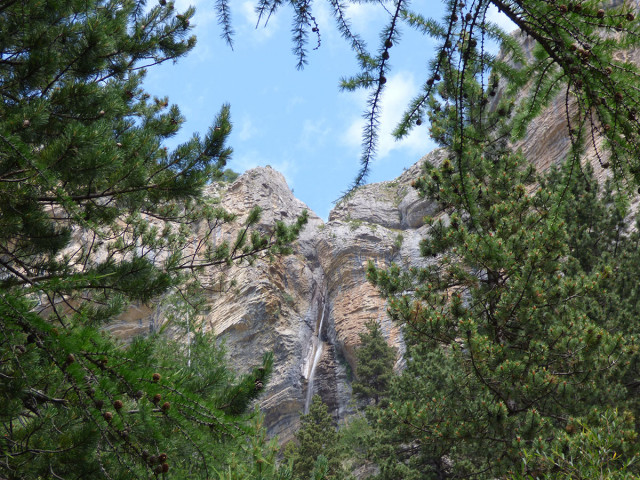 Vue de la cascade du Pich, située dans une crevasse rocheuse à côté d'une forêt de conifères