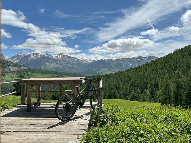 Panorama dégagé de montagnes boisées, VTT posé contre une table d'observation en bois - © Marc Eldin Panorama dégagé de montagnes boisées, VTT posé contre une table d'observation en bois