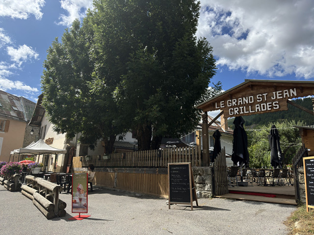 Restaurant terrace overlooking the main street of Allos, and a private outdoor terrace with tables and chairs. Sign 
