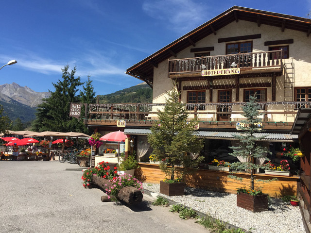 Exterior of the hotel, a three-story chalet with a flower-filled terrace. Hotel frontage. Mountain views in summer.