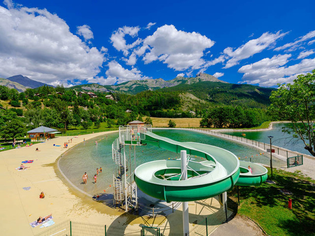 Bassin de baignade du parc de loisirs d'Allos, comportant un toboggan. En arrière-plan, montagnes boisées
