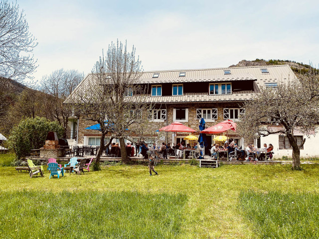View of the restaurant in summer, a large 3-story stone building, outdoor terrace with tables and chairs, in a meadow setting