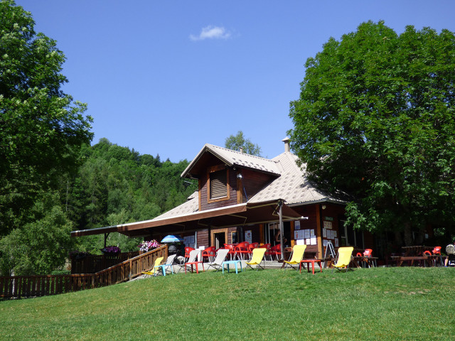 Overview of the Leisure Park restaurant, a two-story wooden building with a terrace (tables, chairs, deck chairs), in a forest setting