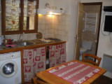Coin séjour avec cuisine, table à manger, évier, machine à laver, carrelage au mur, ameublement bois, porte vers salle de bains