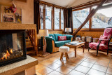 Séjour chaleureux et lumineux avec canapé, fauteuils, cheminée, fenêtres donnant sur le village