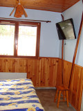 Vue sur un coin de chambre à coucher lumineuse, ameublement en bois, lambris, lit double, TV et fenêtre