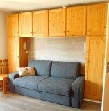 Salon de studio lumineux avec canapé-lit, fenêtre, ameublement bois