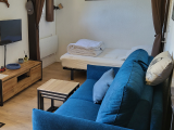 Living area with sofa bed, coffee table and TV, separated by curtains from the bedroom with double bed