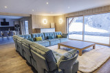 Large, comfortable and bright chalet living room, large corner sofa, rug, coffee table, wooden furniture. Kitchen area with large television and French windows.