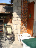 View of an outdoor terrace, wood pile, garden shed with an outdoor chimney used for barbecue, pushchair and outdoor table