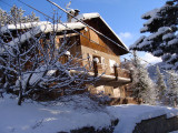 Side view of a three-storey house made out of stone and wood, metal balconies, winter snow-capped scenery