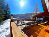 Terrasse en bois du chalet avec grande table d'extérieur, transat, véranda, vue dégagée avec paysage enneigé
