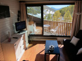 Bright studio living room with sofa, dining table, TV, French doors opening onto a wooden balcony with mountain view