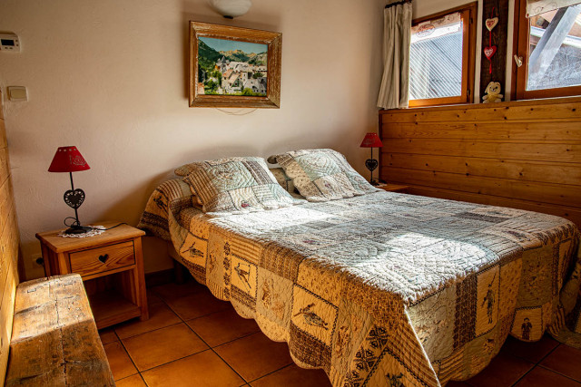 Chambre à coucher lumineuse avec lit double, ameublement en bois et fenêtres donnant sur le village Chambre à coucher lumineuse avec lit double, ameublement en bois et fenêtres donnant sur le village